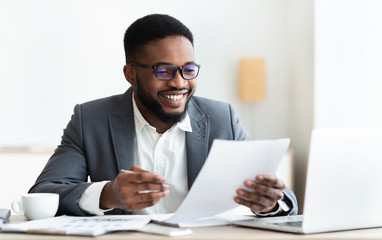 Cheerful black businessman checking reports and making notes