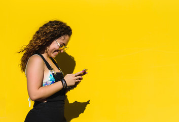 Fototapeta na wymiar young woman typing with a mobile phone while smiling on a yellow background