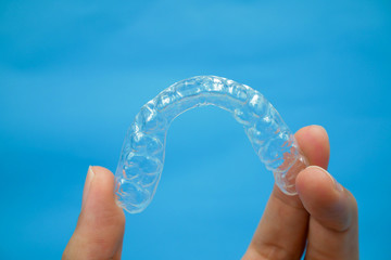 hand holding clear plastic retainer teeth that isolated on blue sky background. it's an equipment for orthodontist give the patient to orthodontic surgery in dental clinic or hospital