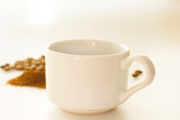 White cup of espresso with coffee grains and ground coffee background. White background with copy space for text. Side view. International Coffee Day