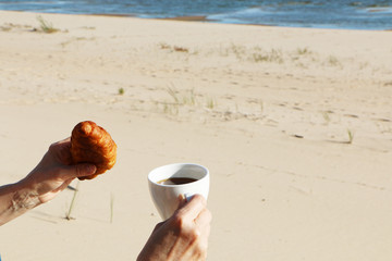 Girl with a croissant and a cup of coffee by the sea