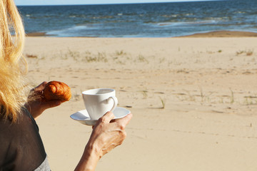 Girl with a croissant and a cup of coffee by the sea