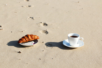 A cup of coffee stands on the sandy seashore