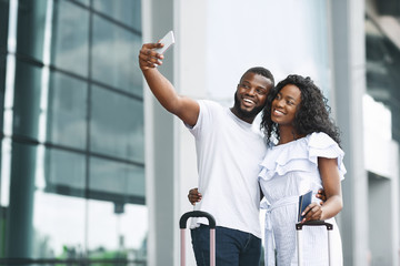 Happy african couple taking selfie, waiting for flight near airport