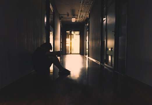 Young Man Sitting Hug His Knee Alone In The Dark On The Walkway At The Office.Sad And Serious Man