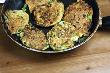 Proper nutrition, vegetarian breakfast gluten free,zucchini courgette pancakes with beans, mint on frying pan with sour greek yogurt, black background, towel, fork, knife on wooden surface