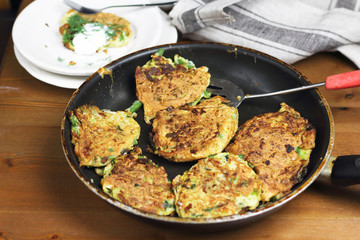 Proper nutrition, vegetarian breakfast gluten free,zucchini courgette pancakes with beans, mint on frying pan with sour greek yogurt, black background, towel, fork, knife on wooden surface