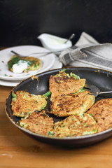 Proper nutrition, vegetarian breakfast gluten free,zucchini courgette pancakes with beans, mint on frying pan with sour greek yogurt, black background, towel, fork, knife on wooden surface