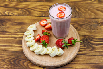 Glass of fresh smoothie of strawberry and banana on a wooden table