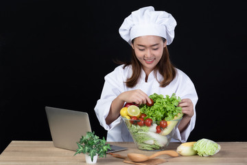 Portrait of a young beautiful Asian woman chef smiling and preparing ingredients for meal or salad by using internet. She was happy and confident .Isolated and studio lighting on black background.