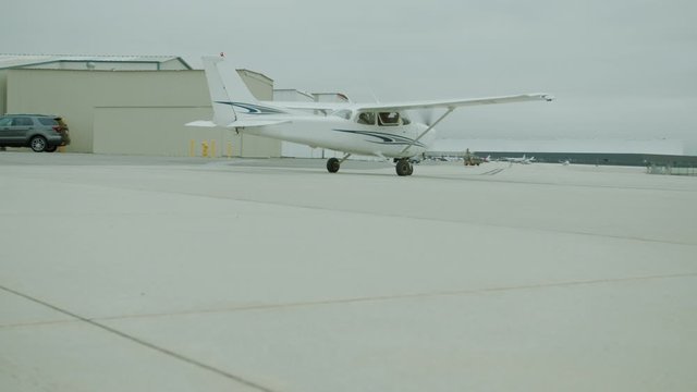 Small generic private propeller airplane preparing for take-off, passing by hangars, no tail or identification number. 60 FPS Slow Motion, 4K RAW graded footage
