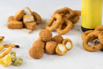 Fast food products: onion rings, french fries, chicken nuggets, olive ascolane, fried mini mozzarella and beer bottle without logo design on white wooden table