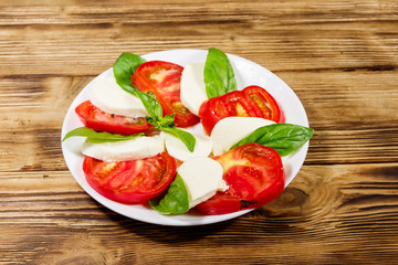 Italian caprese salad with tomatoes, mozzarella cheese and basil on a wooden table
