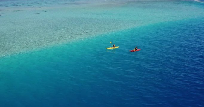 Aerial view of adventurous couple ocean kayaking together in pristine blue lagoon with sunny light textures refracting on the water surface, leisure kayaking tourism