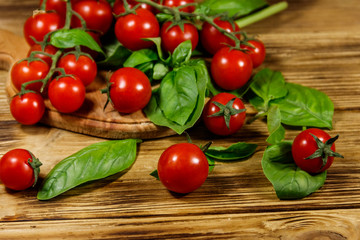 Fresh cherry tomatoes with green basil leaves on a wooden table