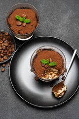 Portion of Classic tiramisu dessert in a glass cup on dark concrete background