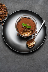 Portion of Classic tiramisu dessert in a glass cup on dark concrete background
