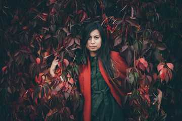 Dreamy beautiful girl with long natural black hair on autumn background of green red grape hedge....
