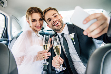 attractive bride and handsome bridegroom taking selfie in car