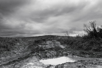 Dirt road after heavy rain leading to the top of the hill, stormclouds on the dark sky in black and white.