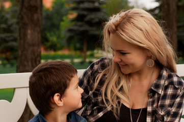 Fototapeta premium Young mother on a bench in the park with her son. Happy moment. Love and motherhood.