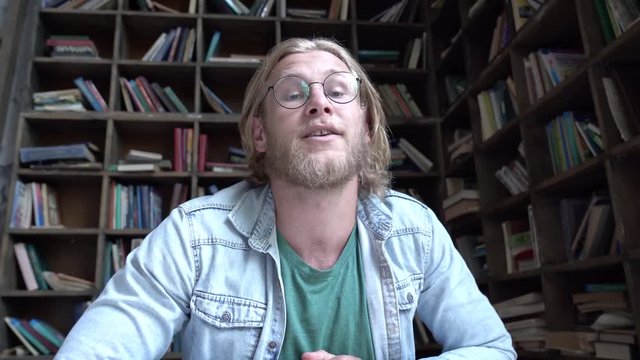 Happy young man student blogger vlogger looking talking to camera in library shooting educational vlog concept, modern male influencer youtuber recording video blog course for youtube channel concept