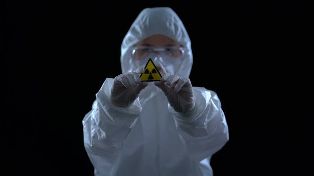 Scientist in protective suit showing ionizing radiation sign, black background