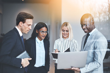 Diverse businesspeople standing in an office using a laptop