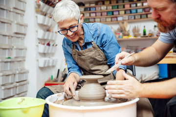 Senior woman spinning clay on a wheel with teacher at pottery class