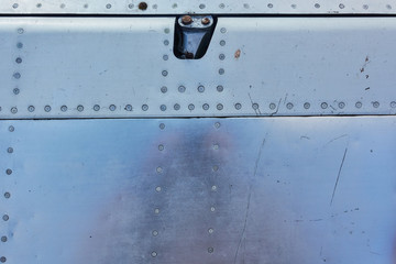 Aluminum surface of the aircraft fuselage. Smooth rows of rivets, there are scratches, dirt