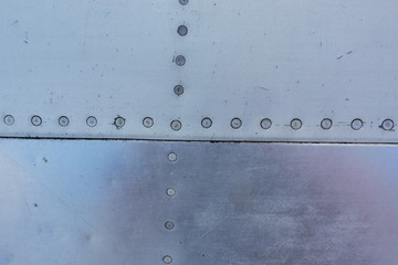Aluminum surface of the aircraft fuselage. Smooth rows of rivets, there are scratches, dirt