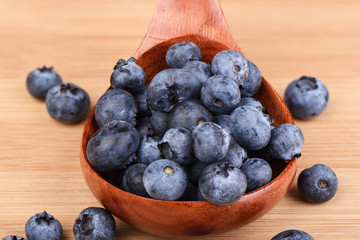 Blueberry berries in a wooden spoon on a wooden background.