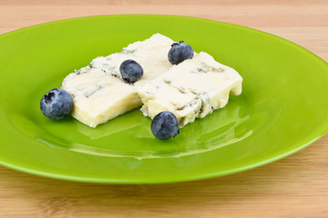Blueberries on slices of delicious blue mold cheese on a green plate.