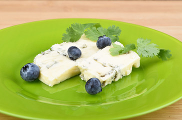 Blueberries and cilantro leaves on slices of delicious blue mold cheese on a green plate.