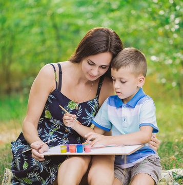 Mother and little son together drawing picture using colourful paints. Horizontal color photography.