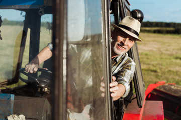 Fototapeta na wymiar selective focus of cheerful senior farmer driving tractor