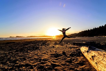 Woman having fun jumping on the beach in the sand during the sunset, trees and mountains in the background