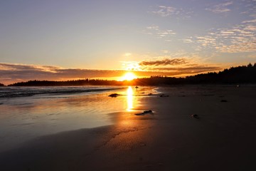 Silhouettes walking on the edge of the ocean at sunset, feet in the sand