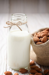 Obraz na płótnie Canvas Milk or yogurt in glass bottle on white wooden table with almonds in hemp sack aside