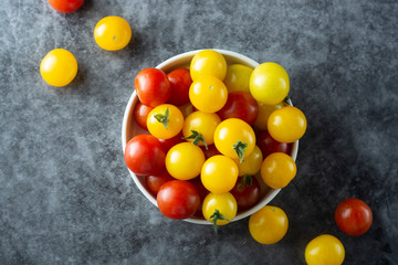 Yellow and red tomatoes in plate, isolated over dark background.