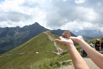 The woman is holding a stone in her hands. In the background is Świnica and a mountain range