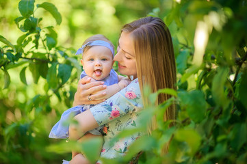 Happy mom walks with a funny baby in a beautiful park at sunset, holds in her arms and have fun