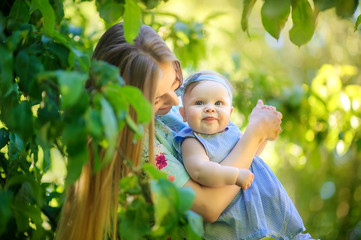 Happy mom walks with a funny baby in a beautiful park, holds in her arms and have fun