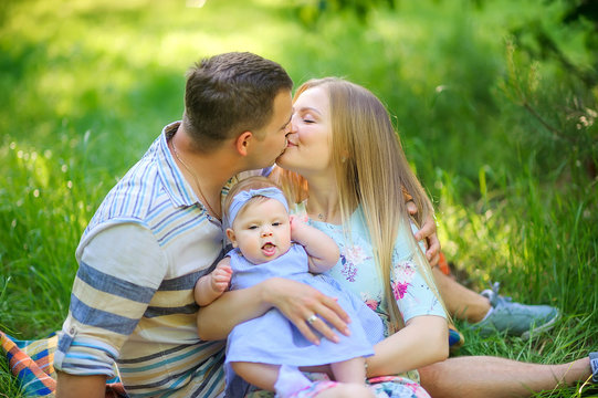 Happy young family is relaxing outdoors. Sitting on the grass in the park hugging and kissing