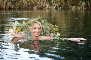 Close-up woman middle-aged blonde wreath of wildflowers on her head swims in the lake, selective focus