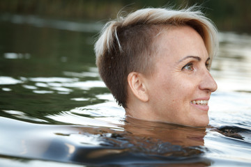 Close-up of a woman blonde middle-aged nude swims in the river, selective focus