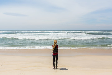 Young woman with blonde long dreadlocks standing by the ocean.