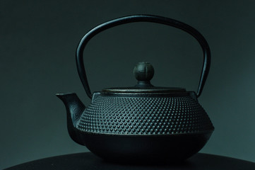 Black textured cast iron kettle on black surface on dark background