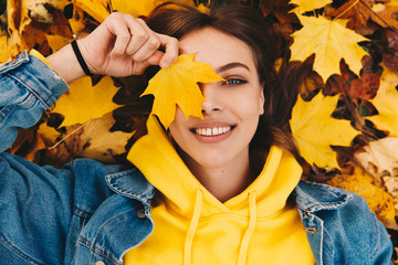 Autumn walk. Woman portrait. Happy girl in yellow hoodie and jean jacket is playing with leaf,...