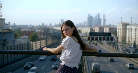 young woman stands on trestle over cars driving in street